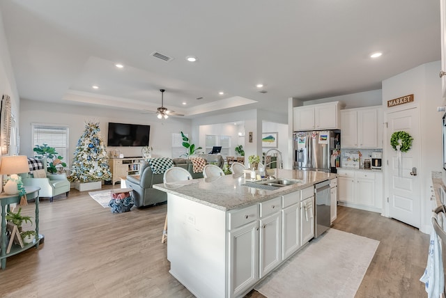 kitchen featuring appliances with stainless steel finishes, a tray ceiling, a kitchen island with sink, and sink