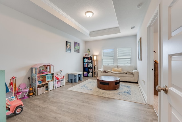 recreation room with light hardwood / wood-style floors, ornamental molding, a textured ceiling, and a tray ceiling