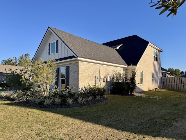 view of home's exterior featuring a shingled roof, fence, a yard, board and batten siding, and brick siding