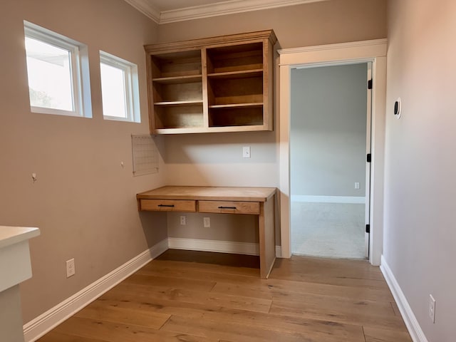 unfurnished office featuring ornamental molding, built in desk, light wood-type flooring, and baseboards