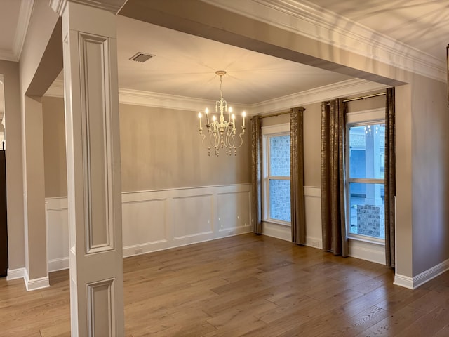 unfurnished dining area with a notable chandelier, wood finished floors, visible vents, ornamental molding, and wainscoting