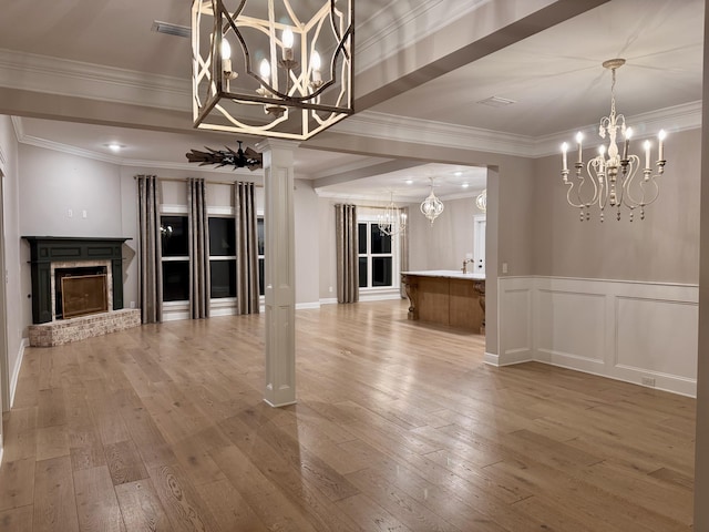 unfurnished dining area featuring light wood-style flooring, a decorative wall, a fireplace, an inviting chandelier, and crown molding