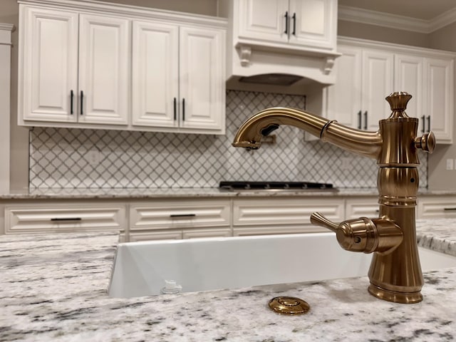 kitchen with tasteful backsplash, light stone countertops, white cabinets, and crown molding