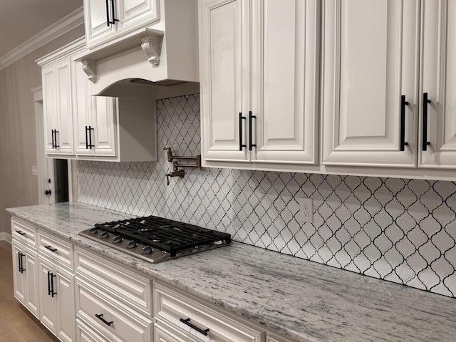 kitchen with stainless steel gas cooktop, white cabinetry, decorative backsplash, light stone countertops, and crown molding