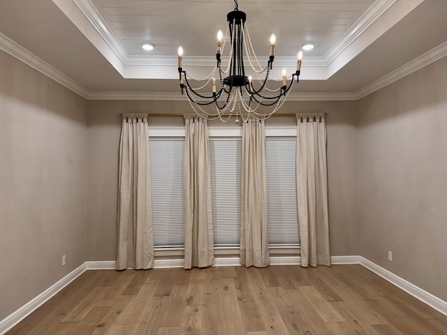 empty room with hardwood / wood-style flooring, baseboards, a raised ceiling, and ornamental molding