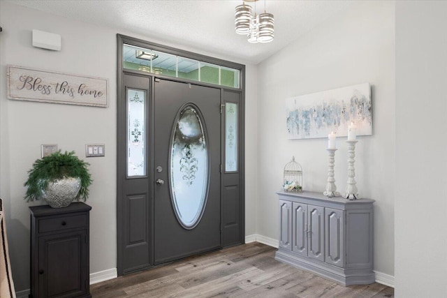 foyer entrance featuring an inviting chandelier, lofted ceiling, a textured ceiling, and light wood-type flooring