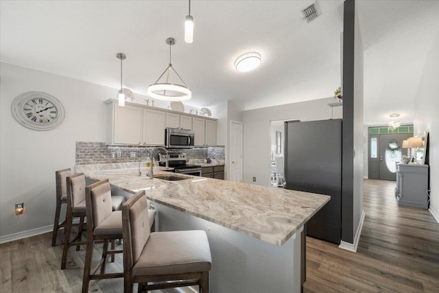 kitchen featuring sink, hanging light fixtures, stainless steel appliances, kitchen peninsula, and a breakfast bar