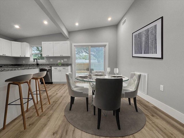 dining area featuring vaulted ceiling with beams, sink, and light wood-type flooring