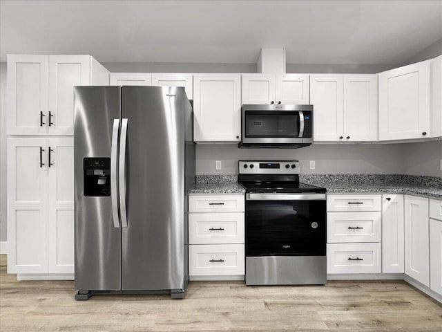 kitchen featuring appliances with stainless steel finishes, light wood-type flooring, dark stone counters, and white cabinets