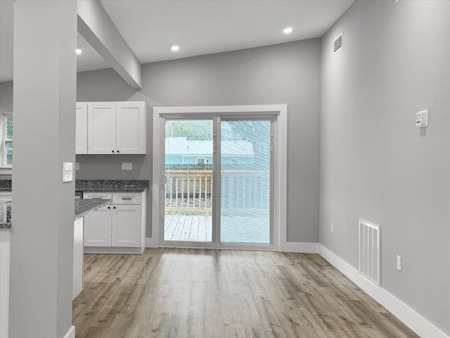 interior space with white cabinetry, light wood-type flooring, and dark stone countertops