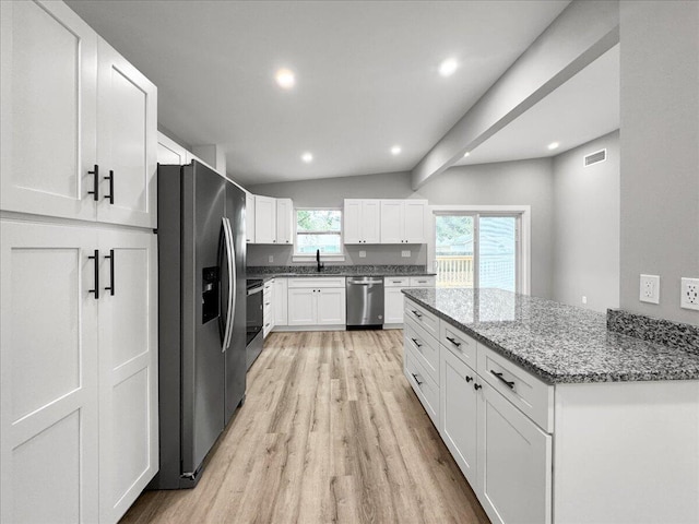 kitchen featuring lofted ceiling, white cabinetry, dark stone countertops, stainless steel appliances, and light hardwood / wood-style floors