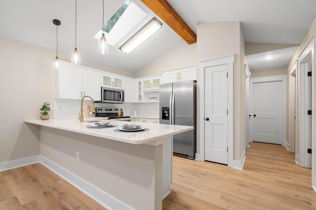 kitchen featuring kitchen peninsula, lofted ceiling with skylight, decorative light fixtures, white cabinets, and appliances with stainless steel finishes