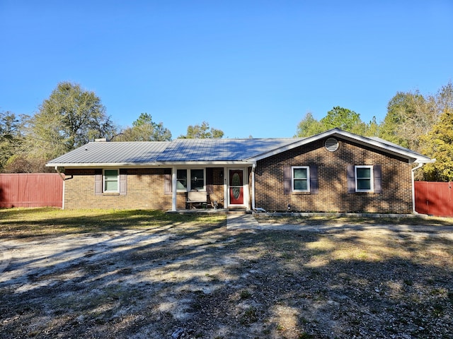 ranch-style house with metal roof, brick siding, and fence