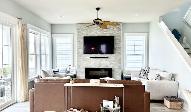 living room with ceiling fan, light hardwood / wood-style floors, and a stone fireplace