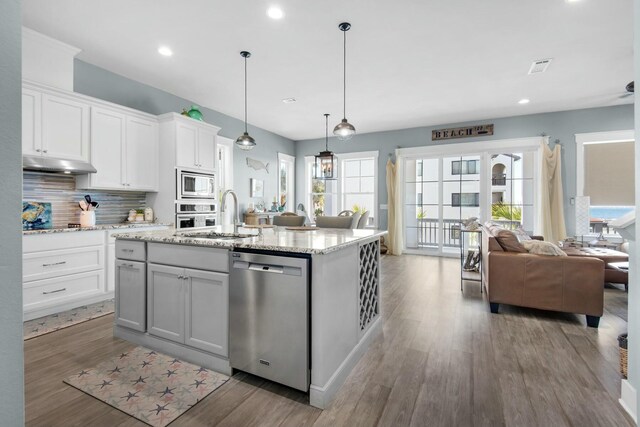 kitchen with stainless steel appliances, a kitchen island with sink, sink, white cabinets, and hanging light fixtures