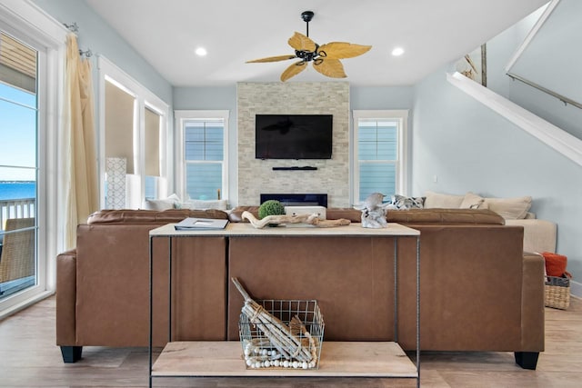 living room featuring light hardwood / wood-style floors, a stone fireplace, and ceiling fan