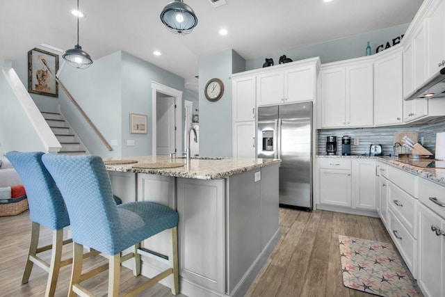 kitchen with sink, stainless steel fridge with ice dispenser, light stone counters, a kitchen island with sink, and white cabinets