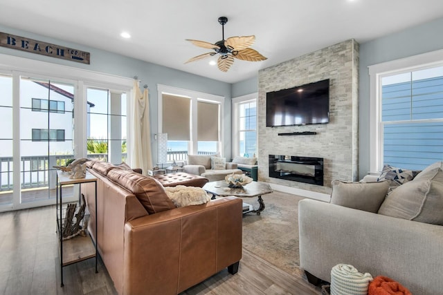 living room featuring a stone fireplace, ceiling fan, and light hardwood / wood-style flooring