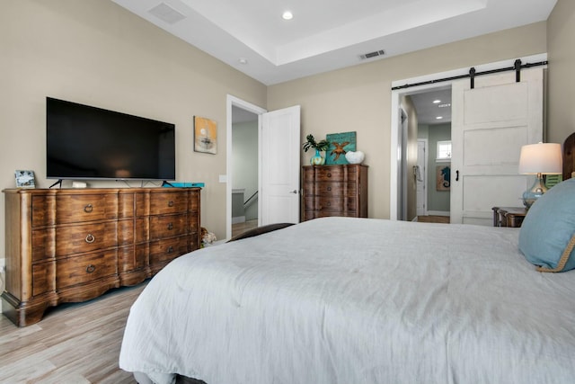 bedroom with a barn door, a tray ceiling, and light hardwood / wood-style floors