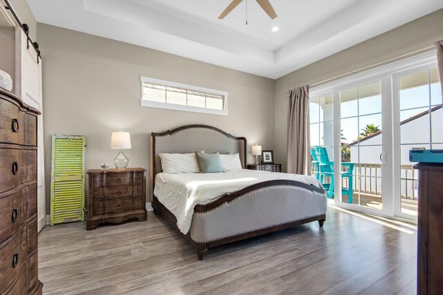 bedroom with a raised ceiling, a barn door, ceiling fan, and access to outside