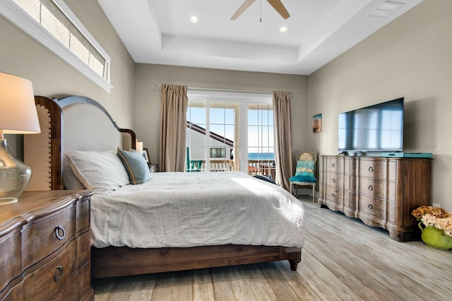 bedroom featuring access to exterior, light wood-type flooring, a raised ceiling, and ceiling fan