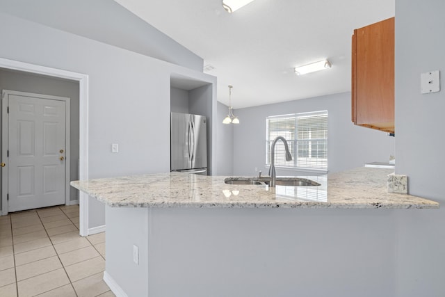 kitchen featuring stainless steel refrigerator, sink, light stone counters, kitchen peninsula, and decorative light fixtures