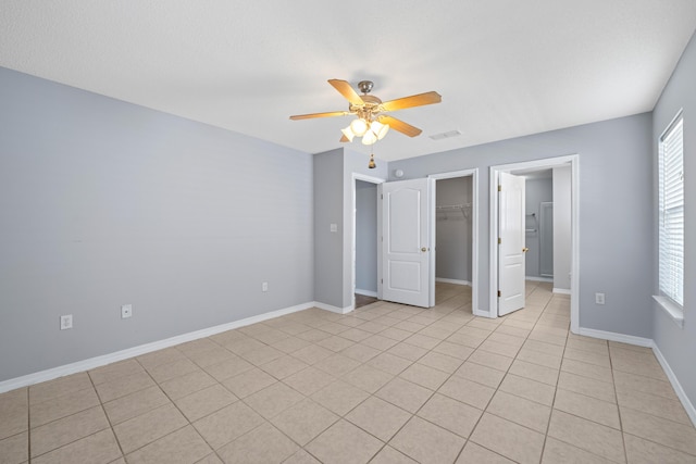 unfurnished bedroom featuring ceiling fan, a walk in closet, light tile patterned floors, and a closet