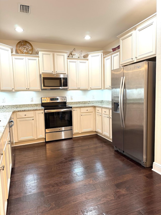 kitchen with dark wood-type flooring, light stone countertops, appliances with stainless steel finishes, and cream cabinets