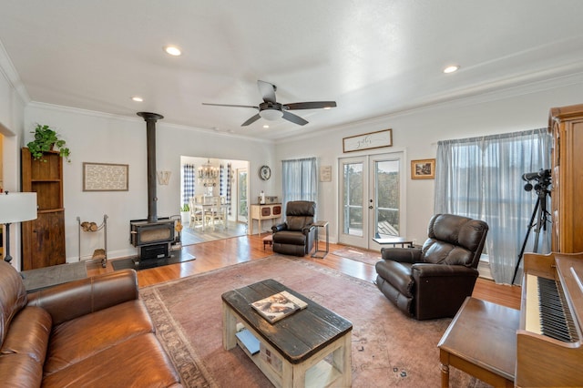 living room featuring french doors, ceiling fan, crown molding, light hardwood / wood-style flooring, and a wood stove