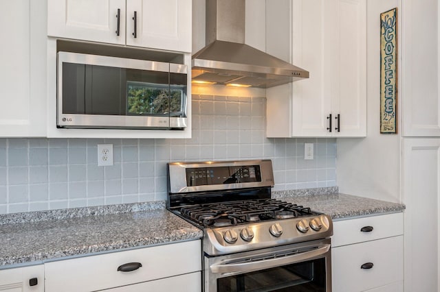 kitchen featuring light stone countertops, appliances with stainless steel finishes, white cabinetry, and wall chimney exhaust hood