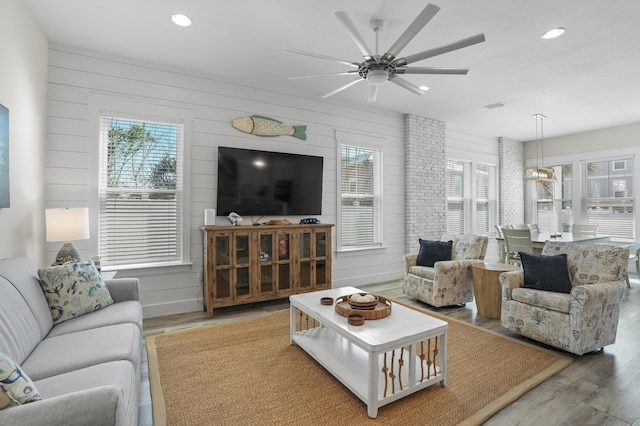 living room with ceiling fan, wood-type flooring, and wood walls