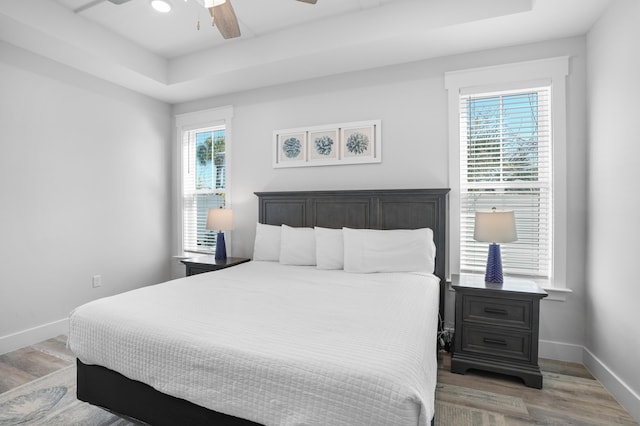 bedroom featuring ceiling fan, wood-type flooring, and a tray ceiling