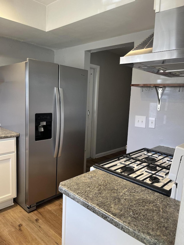 kitchen with stovetop, exhaust hood, stainless steel fridge, light hardwood / wood-style floors, and white cabinets