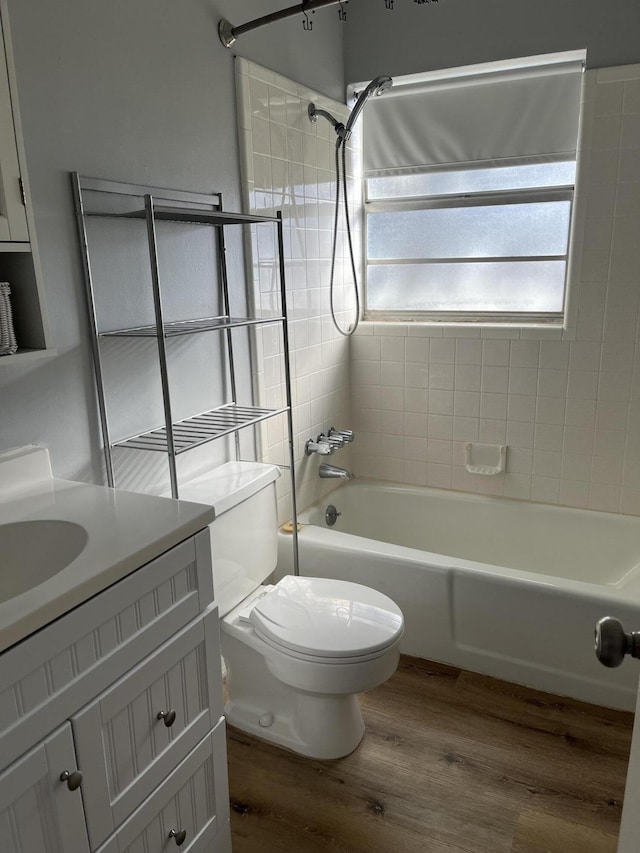 full bathroom featuring hardwood / wood-style floors, tiled shower / bath combo, vanity, and toilet