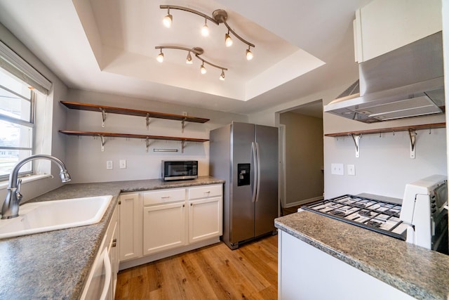 kitchen featuring sink, white cabinetry, appliances with stainless steel finishes, a raised ceiling, and wall chimney range hood