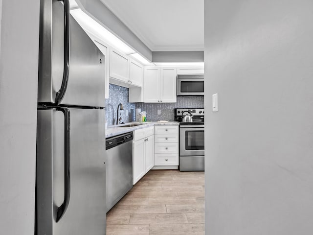 kitchen with sink, stainless steel appliances, tasteful backsplash, white cabinets, and ornamental molding