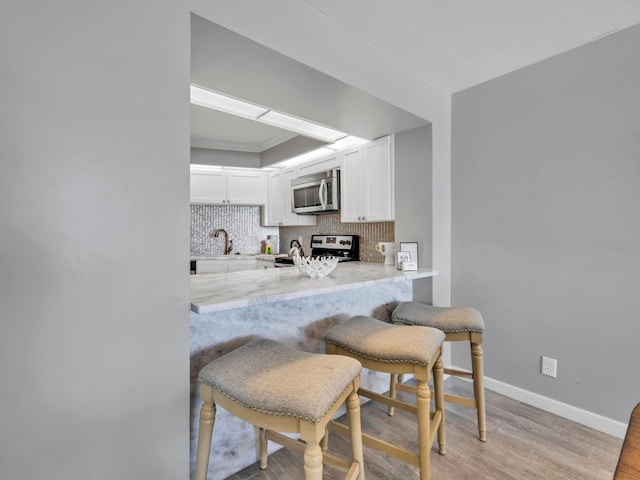 kitchen with a kitchen bar, decorative backsplash, kitchen peninsula, white cabinetry, and range with electric stovetop