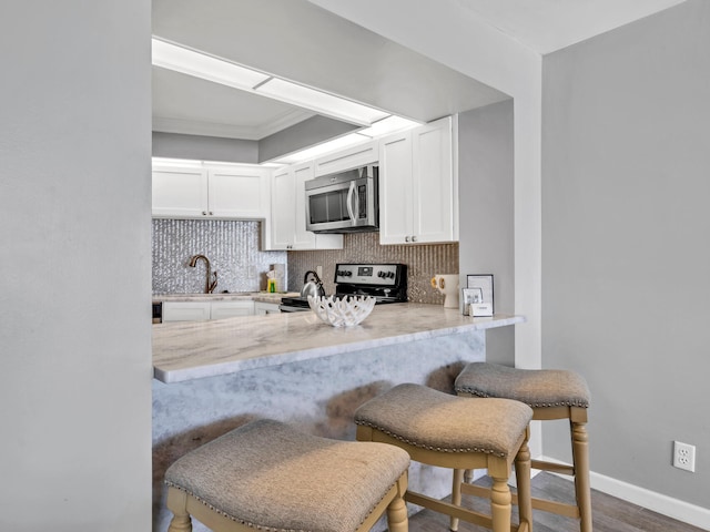 kitchen featuring kitchen peninsula, a breakfast bar, sink, electric stove, and white cabinetry