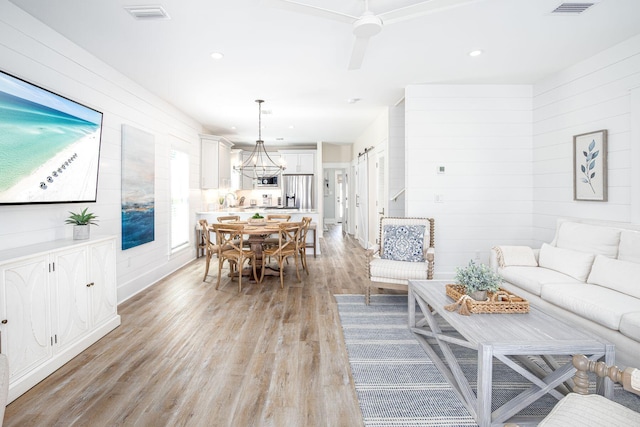 living room with ceiling fan, a barn door, and light wood-type flooring