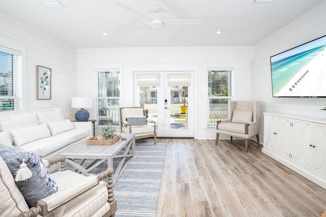 living room with ceiling fan, light hardwood / wood-style flooring, wooden walls, and french doors