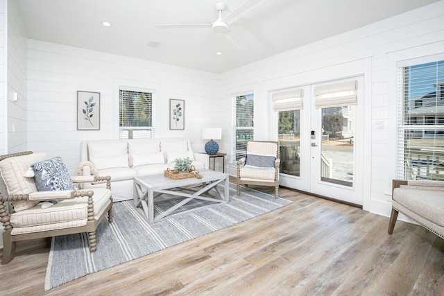 living room featuring wood walls, ceiling fan, light hardwood / wood-style floors, and french doors