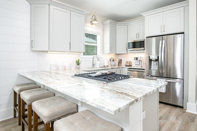 kitchen with kitchen peninsula, light stone countertops, stainless steel appliances, white cabinetry, and a breakfast bar area