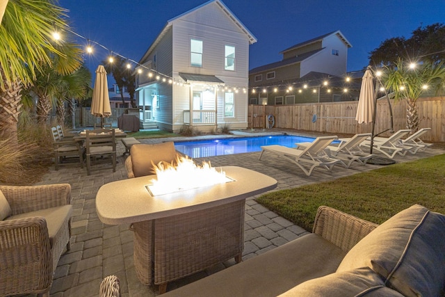 pool at night with a patio area, a yard, and an outdoor fire pit