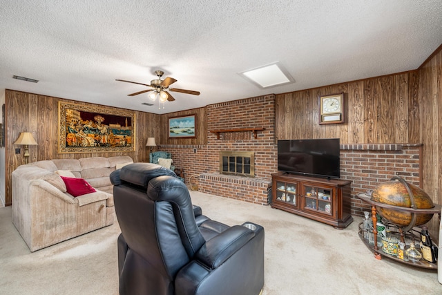 carpeted living room featuring ceiling fan, wooden walls, a brick fireplace, and a textured ceiling