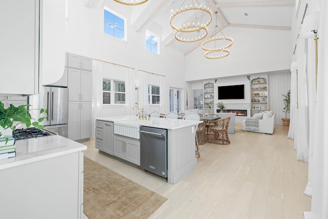 kitchen with gray cabinetry, stainless steel appliances, high vaulted ceiling, an island with sink, and a chandelier