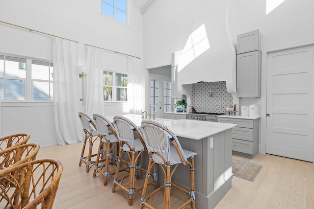 kitchen featuring a center island with sink, a kitchen breakfast bar, light hardwood / wood-style flooring, gray cabinets, and a towering ceiling