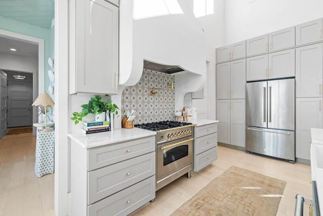 kitchen with gray cabinetry, decorative backsplash, high quality appliances, and light hardwood / wood-style flooring