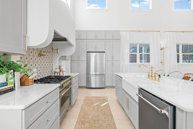 kitchen featuring gray cabinetry, sink, decorative backsplash, a towering ceiling, and stainless steel appliances