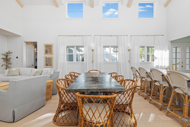 dining room featuring beamed ceiling, a high ceiling, and light wood-type flooring