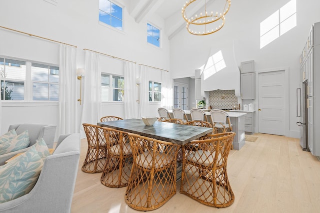 dining space featuring beam ceiling, a towering ceiling, light hardwood / wood-style floors, and an inviting chandelier